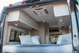 Explore the comfortable interior of this RV rental, featuring a plush bed, overhead cabinets, and AC for a relaxing journey.