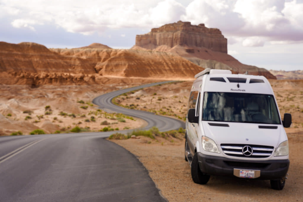 Experience a scenic desert road trip with this white Roadtrek RV rental, winding through unique rock formations.