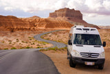 Experience a scenic desert road trip with this white Roadtrek RV rental, winding through unique rock formations.