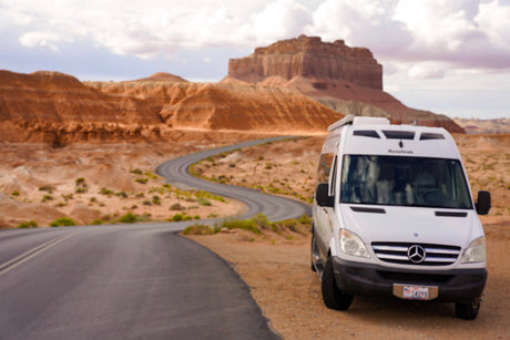 Experience a scenic desert road trip with this white Roadtrek RV rental, winding through unique rock formations.