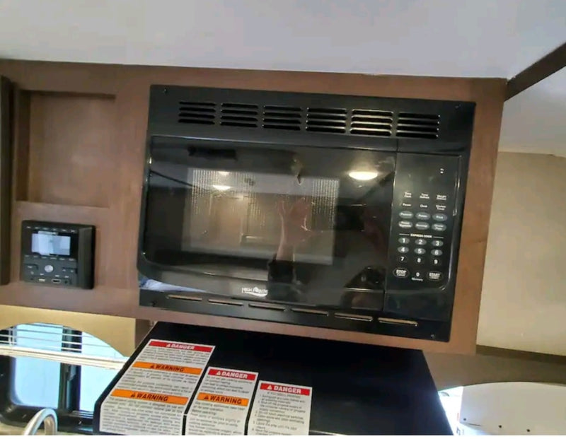 Inside an RV rental: a compact kitchen area with a black built-in microwave and a control panel for amenities. — photo 9