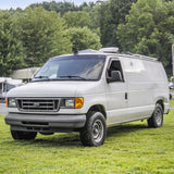 A white Ford van, a rugged van conversion or RV rental camper, parked on grass. Ideal for outdoor adventure.