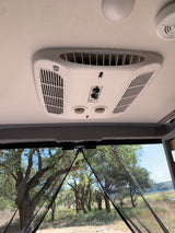RV rental interior showing AC, smoke detector, and a view through mesh screen of trees & a lake.