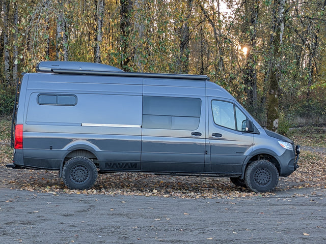 Adventure awaits! Dark gray Sprinter camper van, great for rv rental trips, parked among autumn leaves.