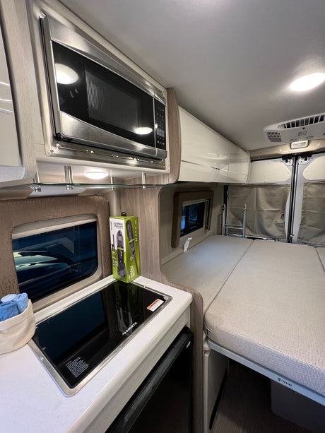 RV rental interior: a compact kitchen with Dometic cooktop & Samsung microwave, alongside a comfortable sleeping area.