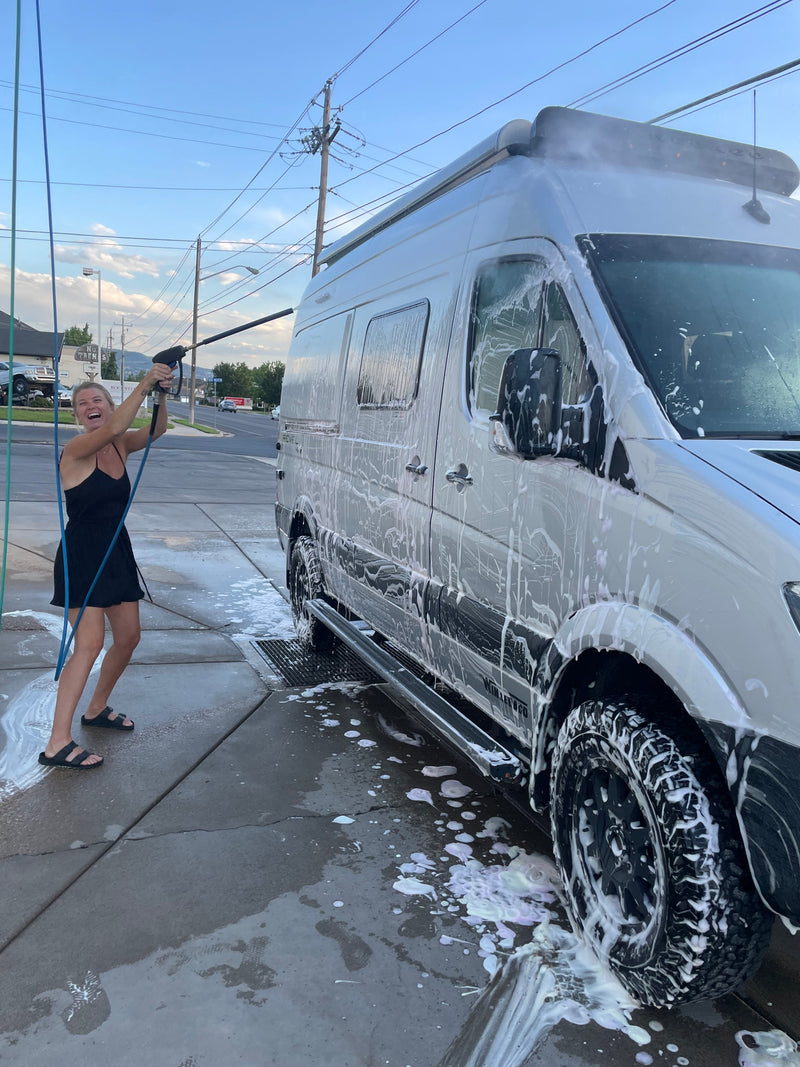 A woman joyfully pressure washing an RV rental covered in suds at an outdoor wash station. — photo 10