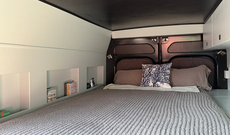 Cozy RV rental interior with a built-in bed, shelving, and overhead storage. Ideal for a comfortable road trip.