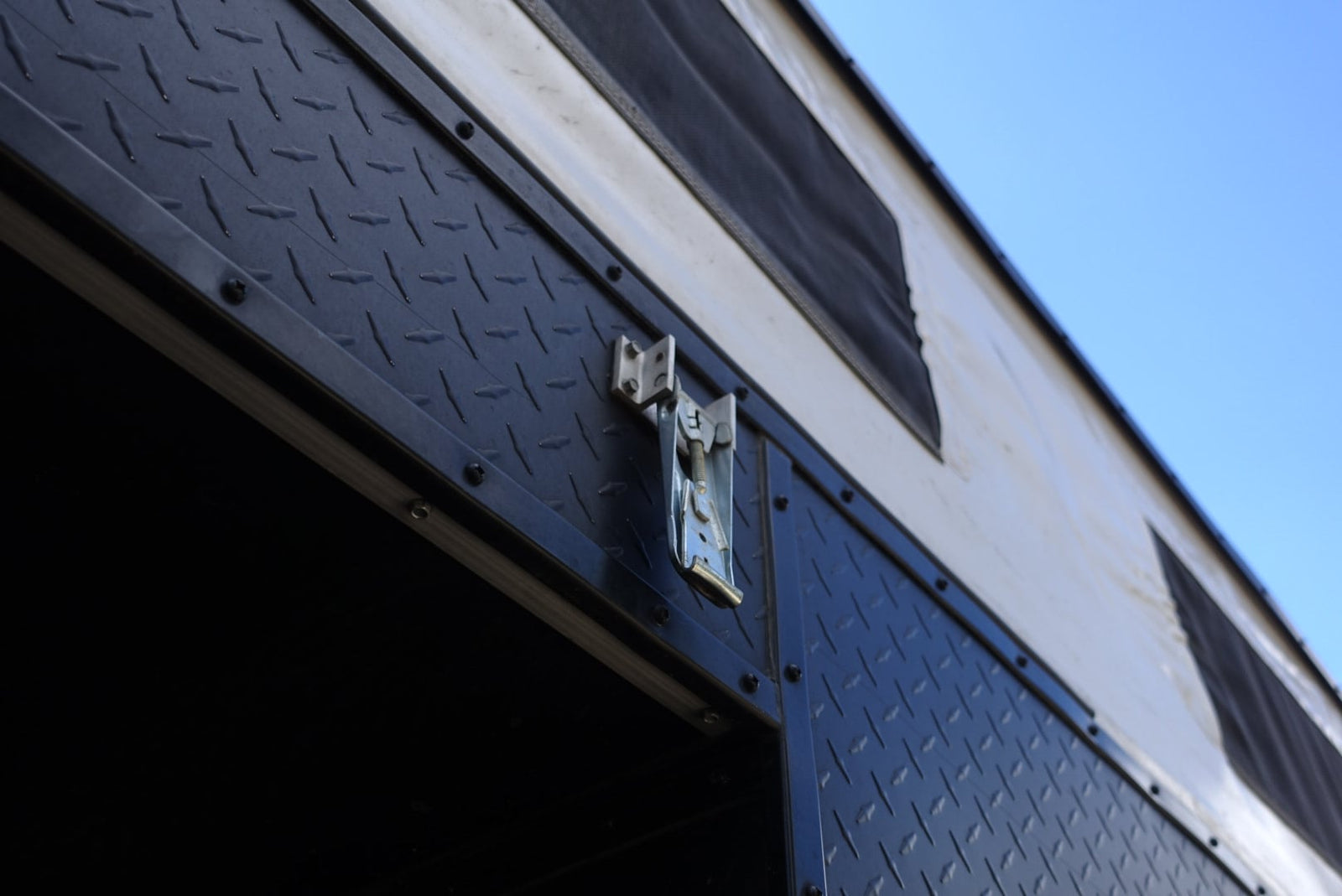 RV rental's exterior featuring a rugged diamond-plate panel, metal latch, and canvas wall with vents against a blue sky.