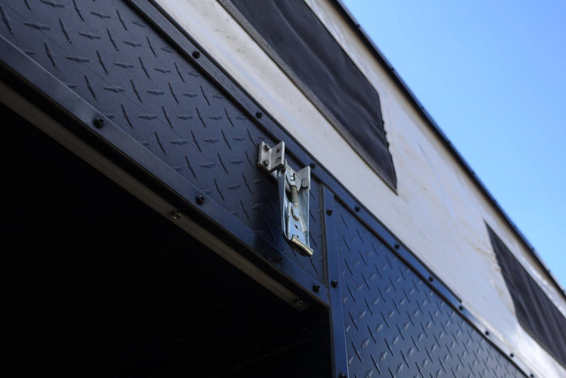 RV rental's exterior featuring a rugged diamond-plate panel, metal latch, and canvas wall with vents against a blue sky. — photo 5