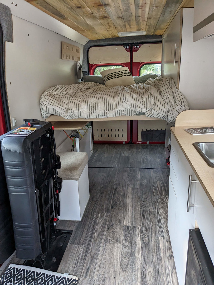  is parked on a dirt road among tall trees. Ideal for camping.|Inside this cozy rv rental van