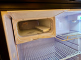 Interior of an RV rental's clean, empty mini-fridge, featuring a small freezer compartment with a container and wire shelves.