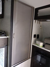 RV rental interior features a grey retractable screen door, compact kitchen with microwave/fridge, and wall controls.