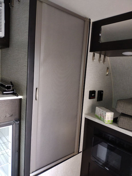 RV rental interior features a grey retractable screen door, compact kitchen with microwave/fridge, and wall controls.