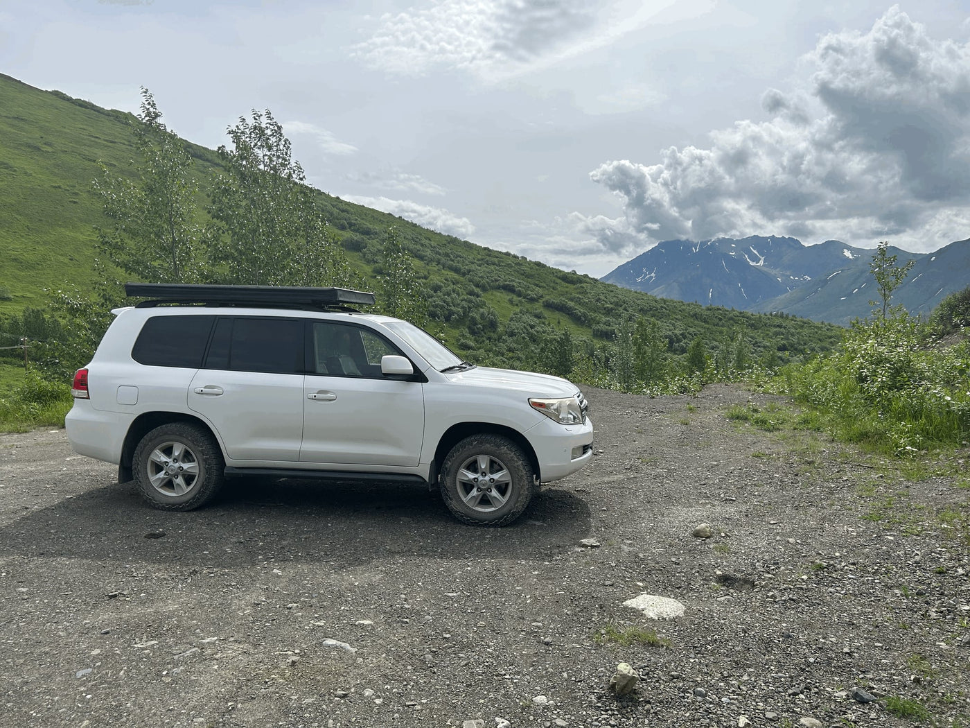  parked on gravel by a green hillside. Ready for overlanding & camping.|RV rental adventure: White SUV with rooftop tent & ladder — photo 3