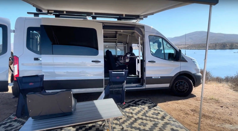 Enjoy lake views with this RV rental camper van, featuring an open side, awning, chairs, and table setup for outdoor living. — photo 9
