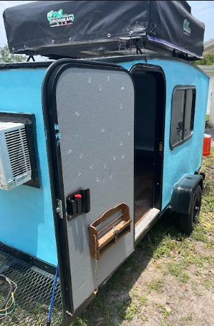 Light blue camper trailer with open door, AC, and a roof-top tent. Ideal for rv rental travel.