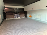 An RV rental bedroom with a large made bed, grey bedding, blue coral pillow, and smart storage for a cozy vibe.