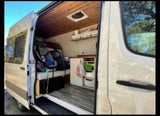 A white camper van rv rental with its side door open, revealing a custom interior, kitchen, and seating area with car seats.