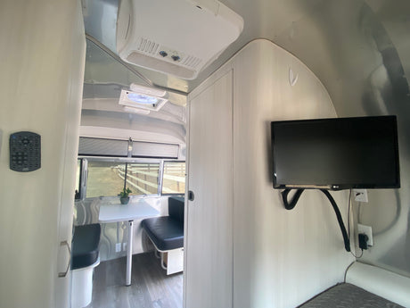 Experience a comfortable RV rental interior with a dinette, wall-mounted TV, and AC unit, showcasing modern amenities.
