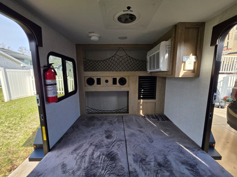 Inside an rv rental, featuring a bed, AC, overhead storage net, and fire extinguisher. Rear door open to outside. — photo 12