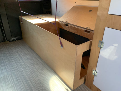 This RV rental interior features custom plywood storage, including an open bed/bench area and hinged compartments.