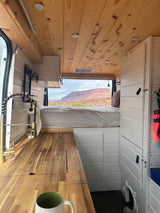 RV rental: Cozy camper van interior features wood kitchen, modern faucet, comfortable bed, and desert mountain view.