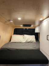 Cozy RV rental bedroom featuring a comfortable bed, natural wood paneling, bright lighting, and built-in storage cabinets.