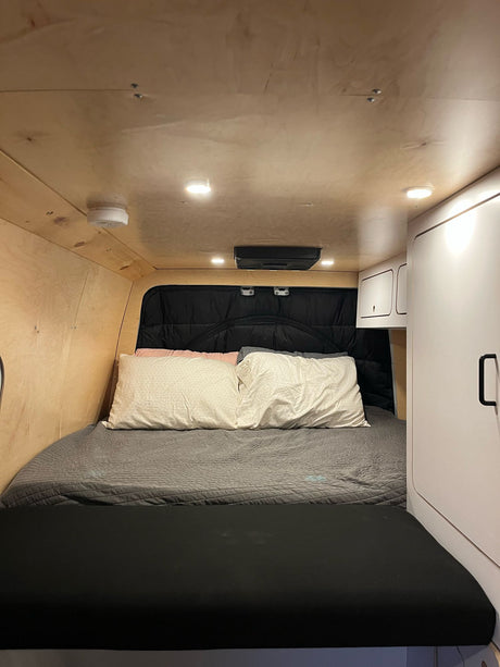 Cozy RV rental bedroom featuring a comfortable bed, natural wood paneling, bright lighting, and built-in storage cabinets.