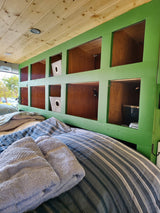 Cozy RV rental interior with custom green-framed storage cubbies, wood paneling, and a striped bed.