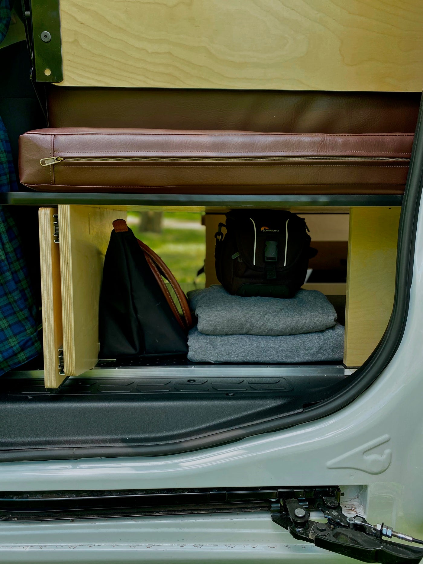 RV rental storage inside: Organized shelves hold a leather cushion, Lowepro camera bag, and blankets in a compact camper van. — photo 8