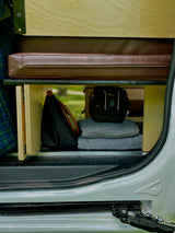 RV rental storage inside: Organized shelves hold a leather cushion, Lowepro camera bag, and blankets in a compact camper van.