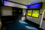 Modern rv rental interior with a cozy bed, TV, AC, and sleek storage. Bright lighting creates a welcoming space.