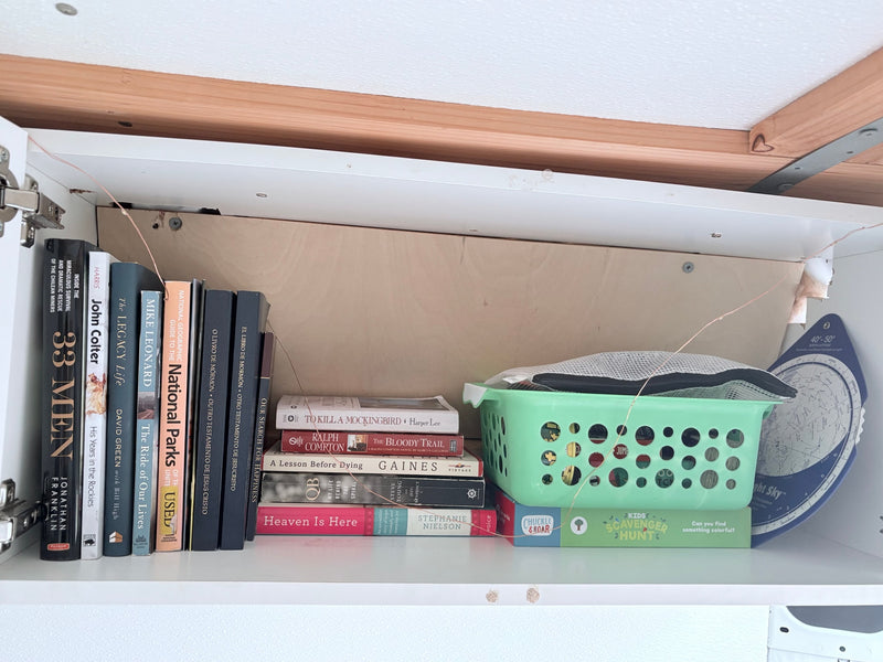 RV rental storage: a neatly organized shelf with books, a green basket, and a night sky chart, brightened by copper string lights. — photo 13