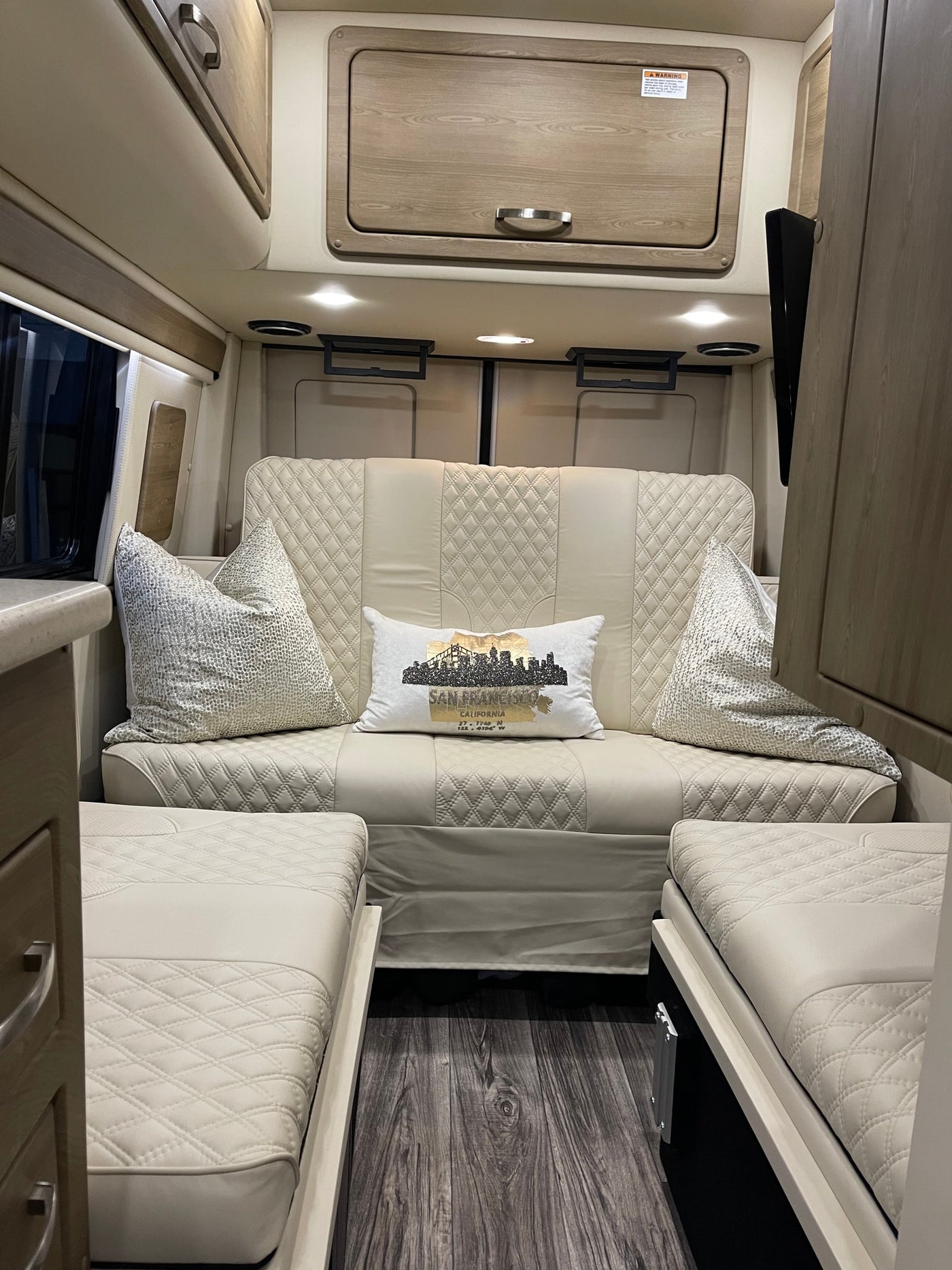 Modern & cozy RV rental interior: quilted sofa/beds, wood-look floor, and sleek overhead storage for your road trip comfort. — photo 15
