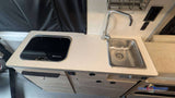 Compact RV rental kitchen features a sink with a faucet, a "Suburban" stovetop, and light-colored counter space.