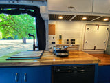 RV rental kitchen view: spacious butcher block counter, induction cooktop, sink, fridge, and green views outside.
