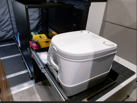 This rv rental features a compact Dometic portable toilet on a slide-out tray, revealing practical storage solutions.