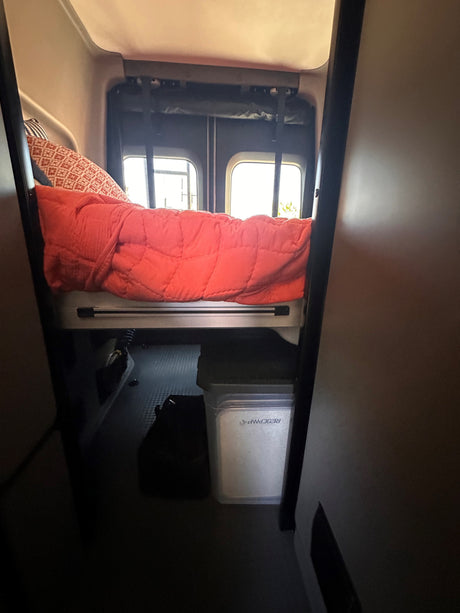 Cozy rv rental interior: comfortable bed with red comforter, patterned pillow, and under-bed storage for mobile living.