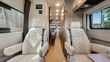 Explore this comfortable rv rental interior. It features cream quilted front seats, a central aisle leading to a rear bed, and large scenic windows.