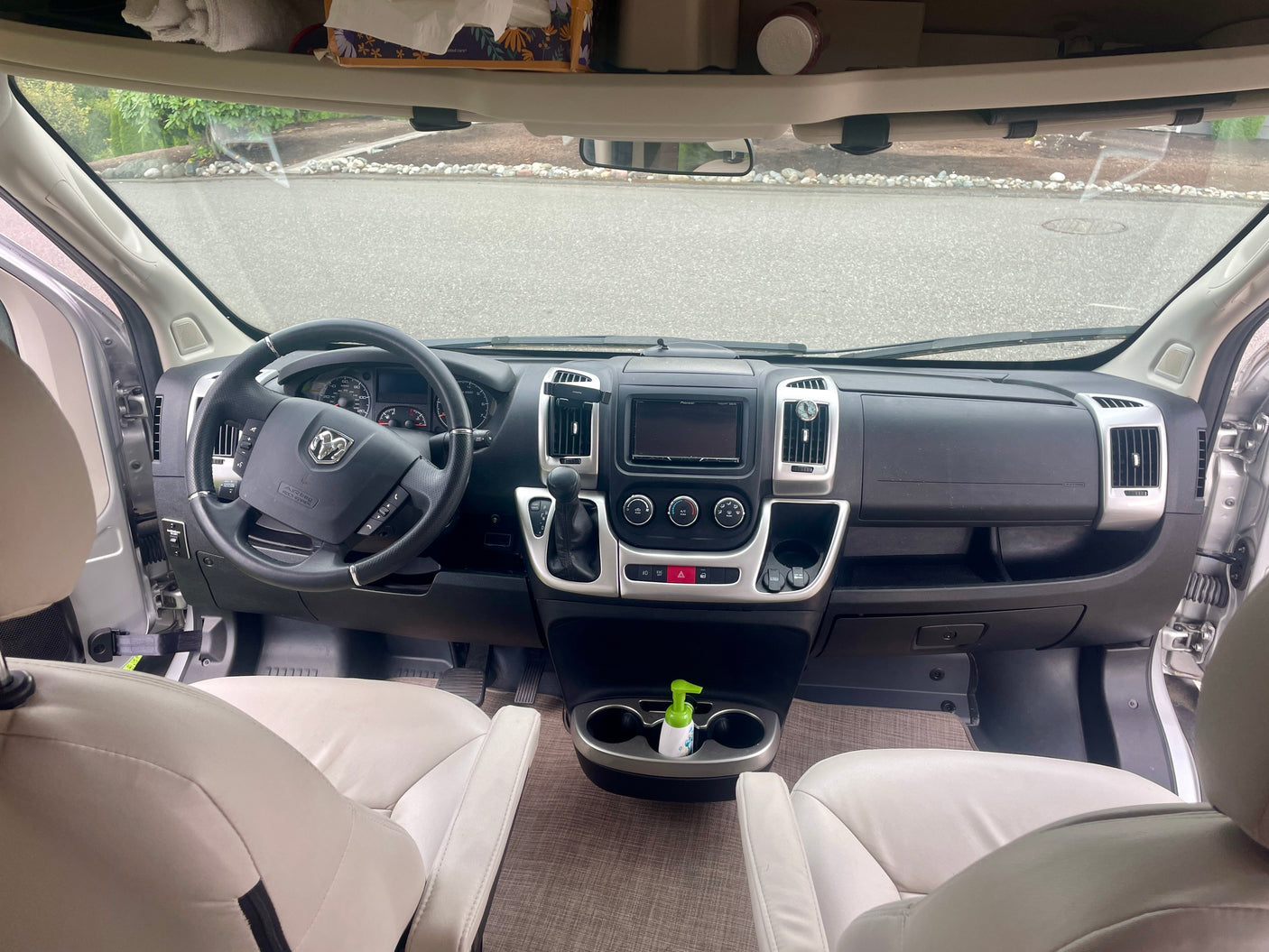 RV rental cabin: Interior view shows a modern dashboard, steering wheel, and front seats, with an overhead storage shelf.