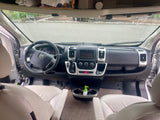 RV rental cabin: Interior view shows a modern dashboard, steering wheel, and front seats, with an overhead storage shelf.