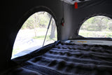 Pop-top RV rental interior: a comfy bed, screened windows, and a view of nature.