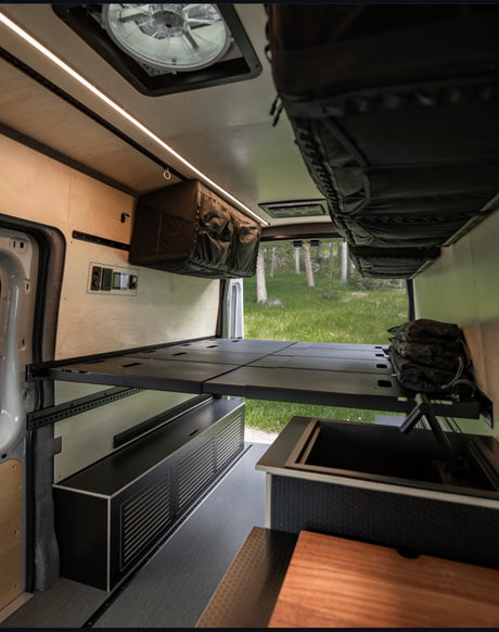 Spacious RV rental interior with a raised bed, modern kitchen sink, and ample storage for comfortable van life adventures.
