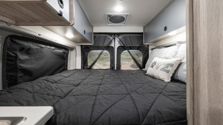 Comfy RV rental bedroom with a paw-print pillow, storage, and scenic lake view through mesh screens.