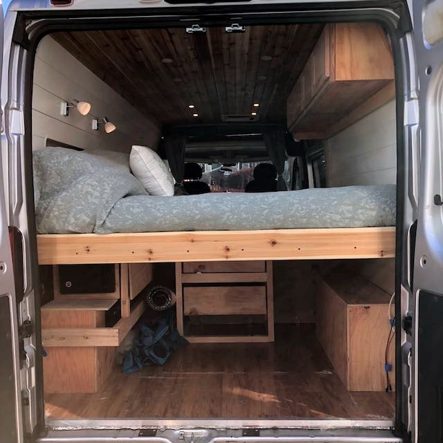 This RV rental showcases a cleverly designed camper van interior with a raised bed, ample storage, and warm wood details.
