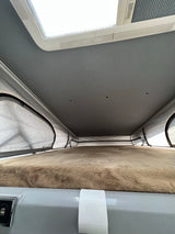 RV rental interior: Upward view of a pop-top sleeping area with furry bed, soft tent walls, ceiling lights, and skylight.