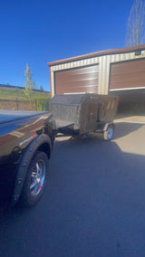 A black truck is hitched to a dark teardrop camper, an RV rental, at a storage facility. Sunny day, units 1 & 2 in background.