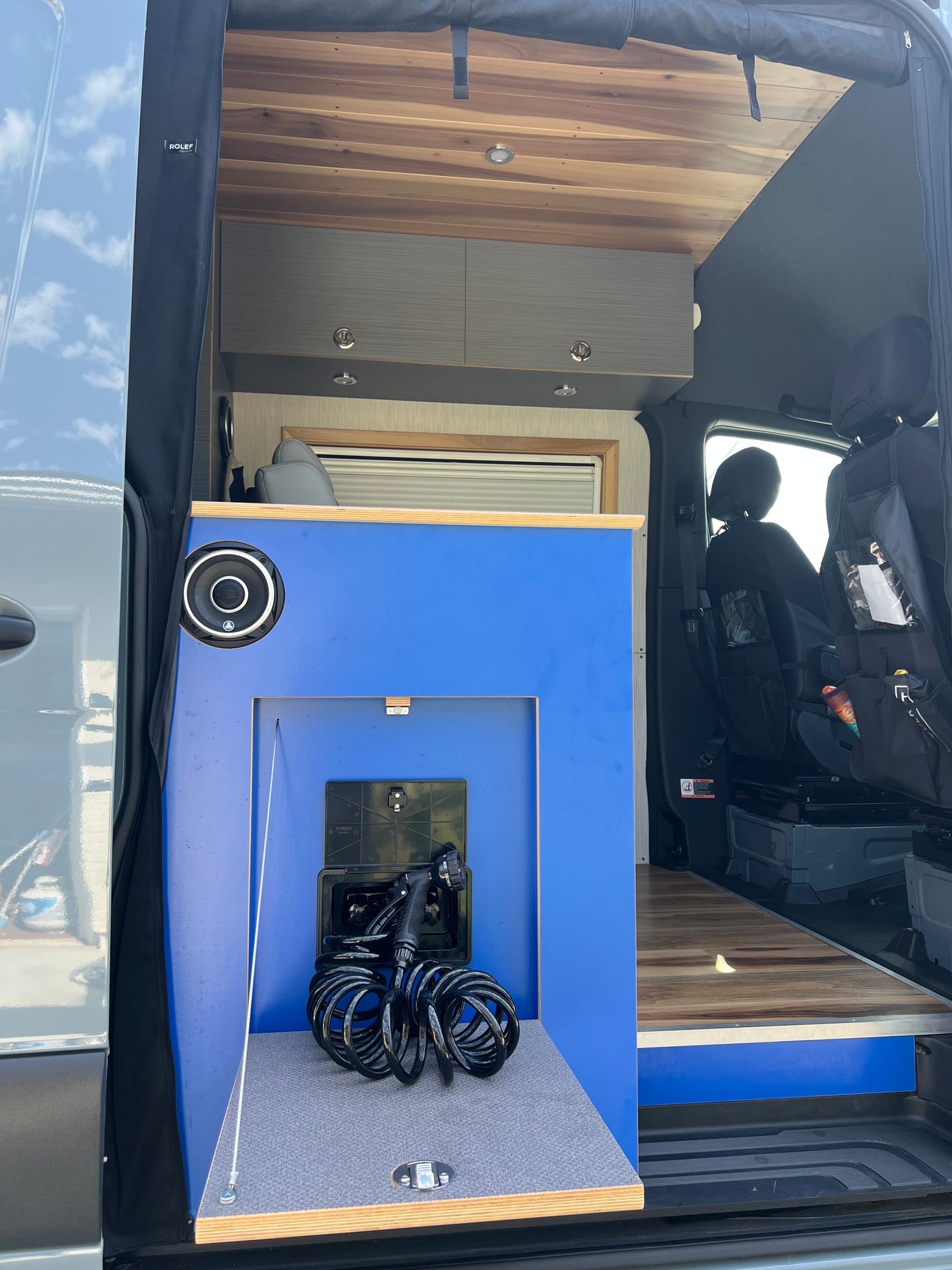 This rv rental's interior features a blue cabinet with a pull-out outdoor shower, overhead storage, and a warm wooden ceiling. — photo 9