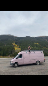 Woman enjoys mountain views from her pink RV rental camper van. Ideal for scenic road trip adventures in nature.