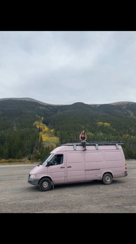 Woman enjoys mountain views from her pink RV rental camper van. Ideal for scenic road trip adventures in nature.